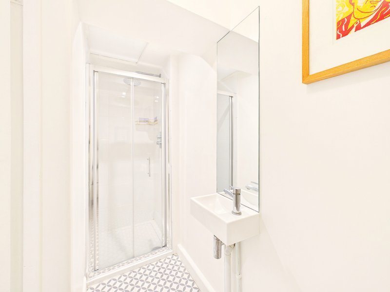 Clean bathroom with shower cubicle, sink, white tiles and framed wall art