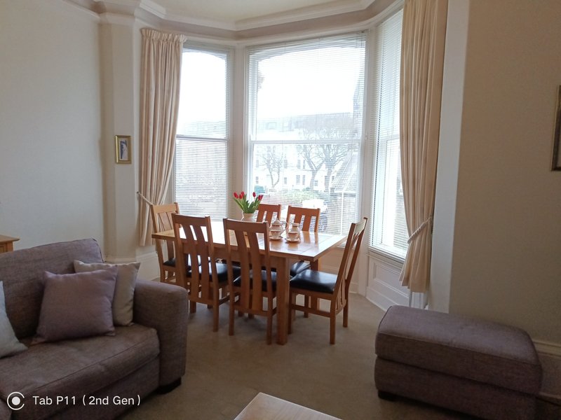 Bright sitting area with dining table, wooden chairs, sofa, bay windows with curtains