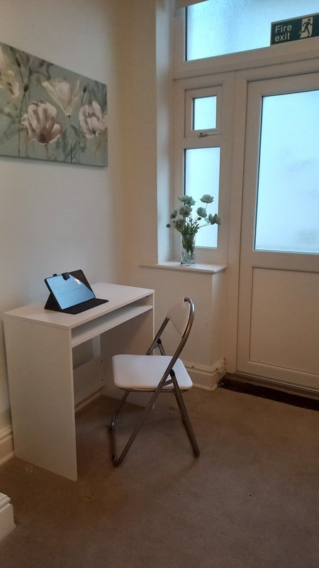 Bright workspace with white desk, wooden chair, laptop, and glass doors leading outside.
