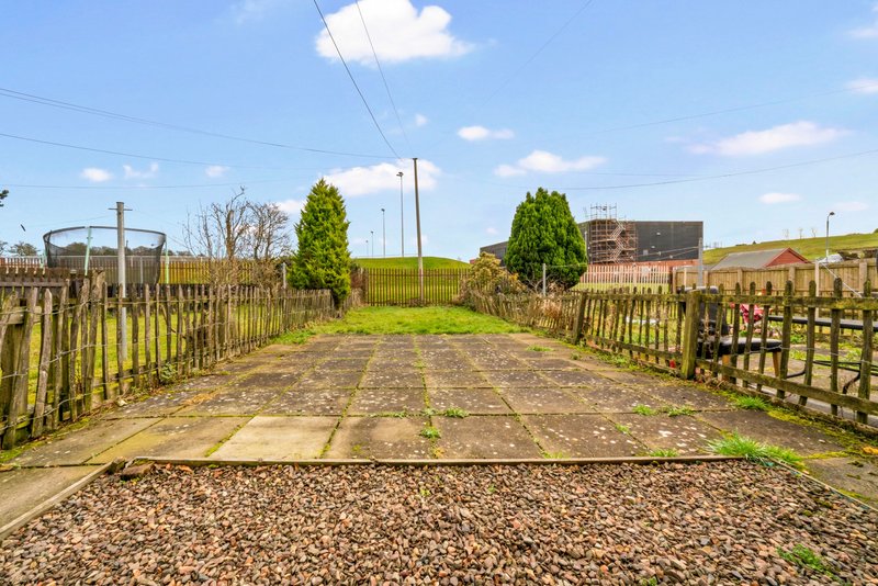 Rural driveway with wooden fencing, gravel surface and distant farmland and buildings