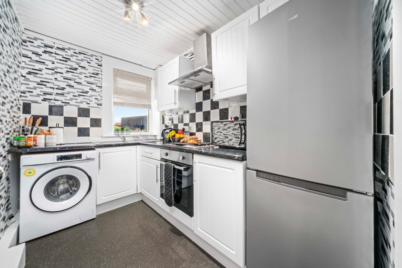 Modern kitchen with white cabinetry, black and white checkered backsplash, stainless steel appliances and washing machine