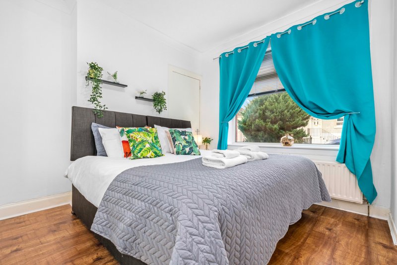 Bedroom with double bed, grey bedding, turquoise curtains and wall-mounted plants