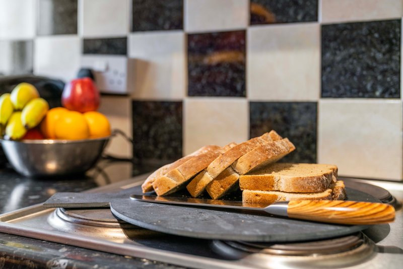 Kitchen countertop with sliced bread on a black board, fresh fruit in bowl, and tiled backsplash
