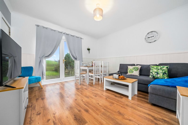 Open-plan living room with sofa, dining table, TV, wooden flooring and garden doors