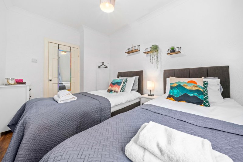 Bright bedroom with two twin beds, dark headboards, white bedding, and wall shelves with plants