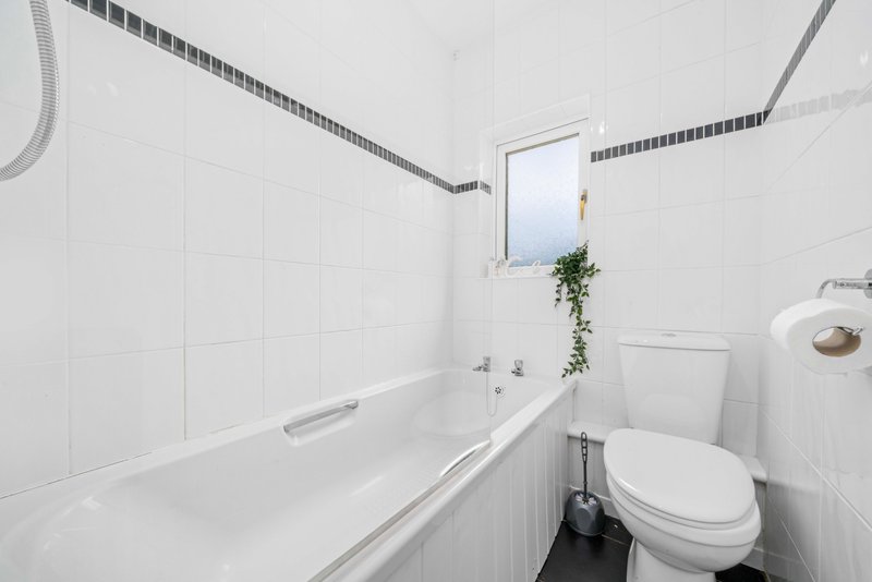 Clean white bathroom with bathtub, toilet, small window and potted plant