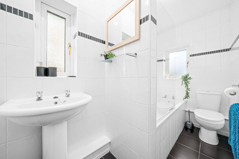 Modern white bathroom with pedestal sink, toilet, bathtub, and dark tile flooring