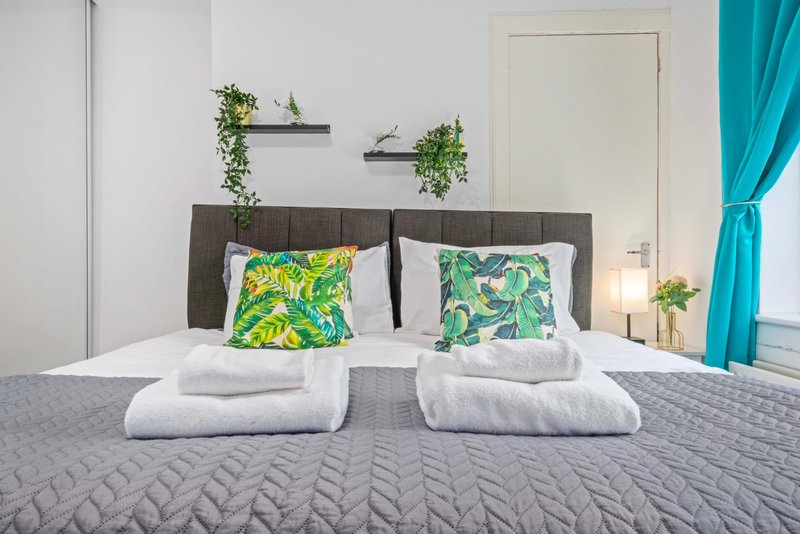 Modern bedroom with double bed, gray headboard, decorative pillows, white towels and potted plants