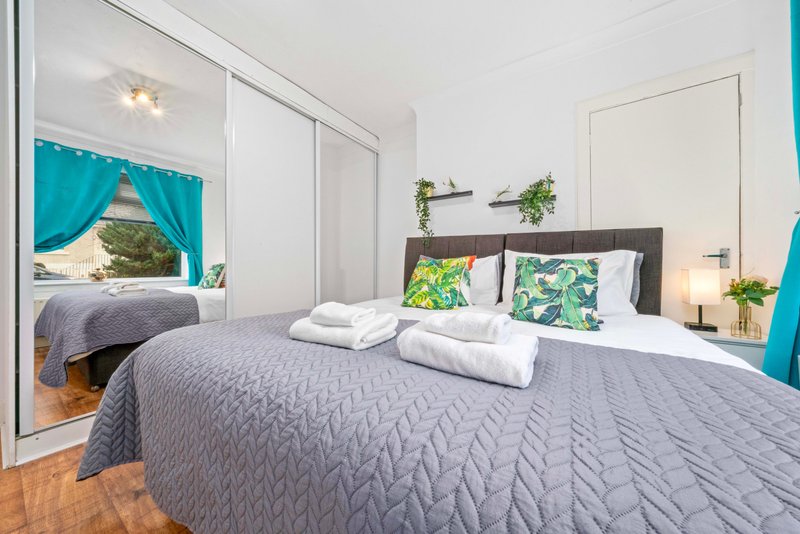 Bright modern bedroom with double bed, grey bedding, patterned pillows, mirror wardrobe and plants