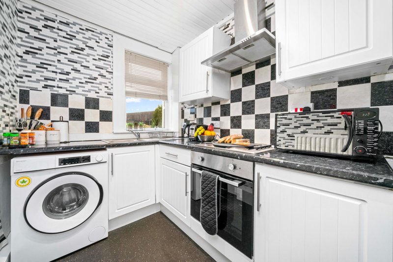 Modern kitchen with white cabinetry, black and white checkered tiles, stove, washing machine and window view