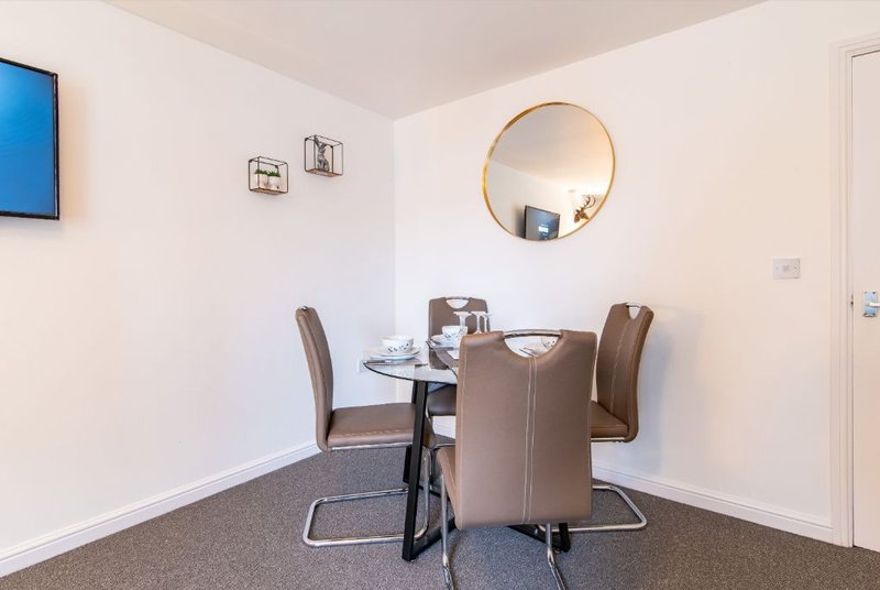 Modern dining area with round glass table, brown upholstered chairs, and gold-framed mirror