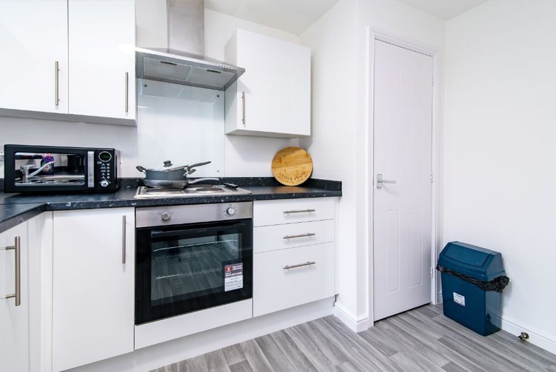 Modern white kitchen with black worktop, built-in oven, microwave, and stainless steel extractor hood