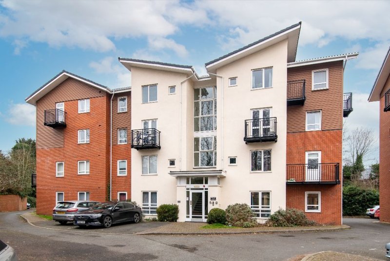 Modern multi-storey residential building with brick and cream facade, parked cars, and landscaping