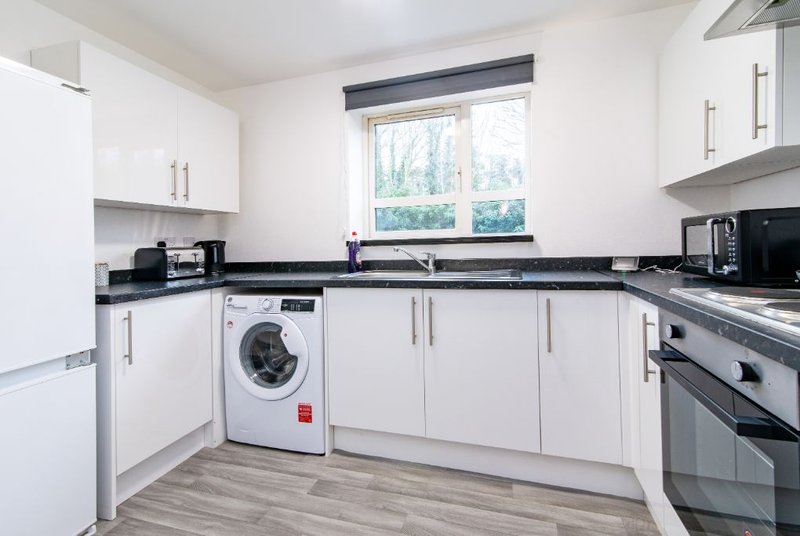 Modern kitchen with white cabinetry, black countertop, integrated appliances and window view