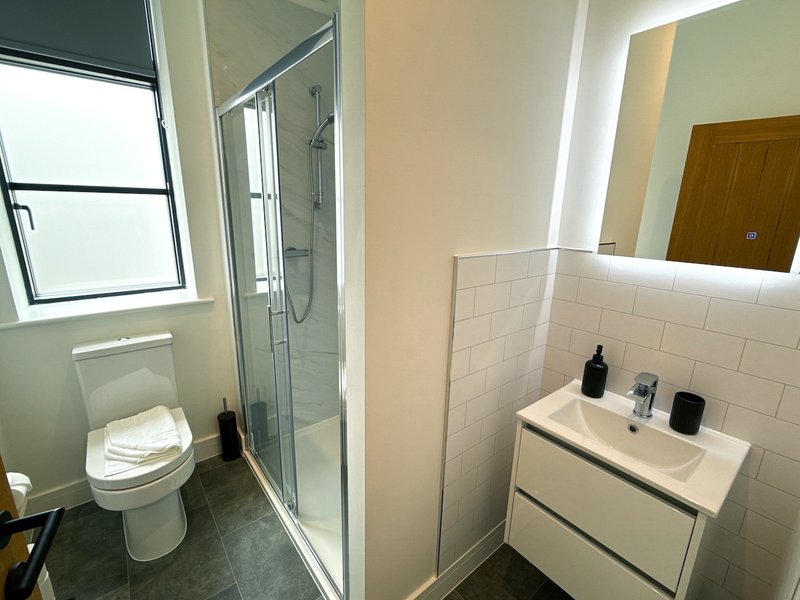 Modern bathroom with toilet, walk-in shower, white tile walls, and vanity sink with mirror