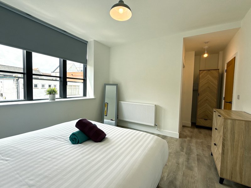 Modern bedroom with double bed, rolled towels, window, radiator and wooden dresser