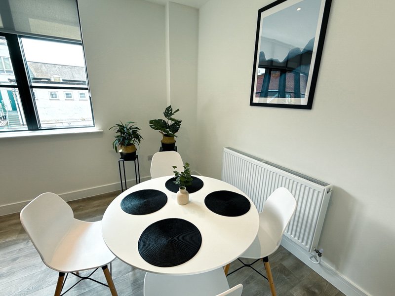 Bright dining area with round white table, black place settings, white chairs and potted plants
