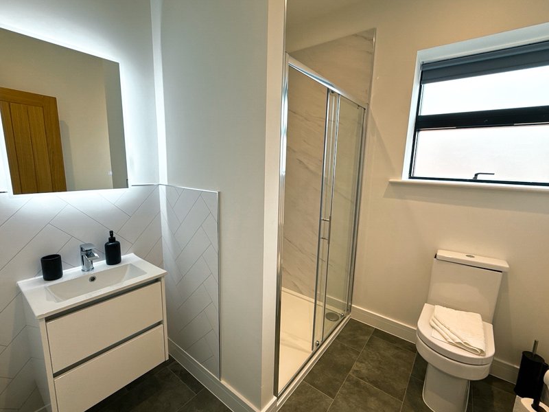 Modern bathroom with white vanity, mirror, shower enclosure, toilet and window