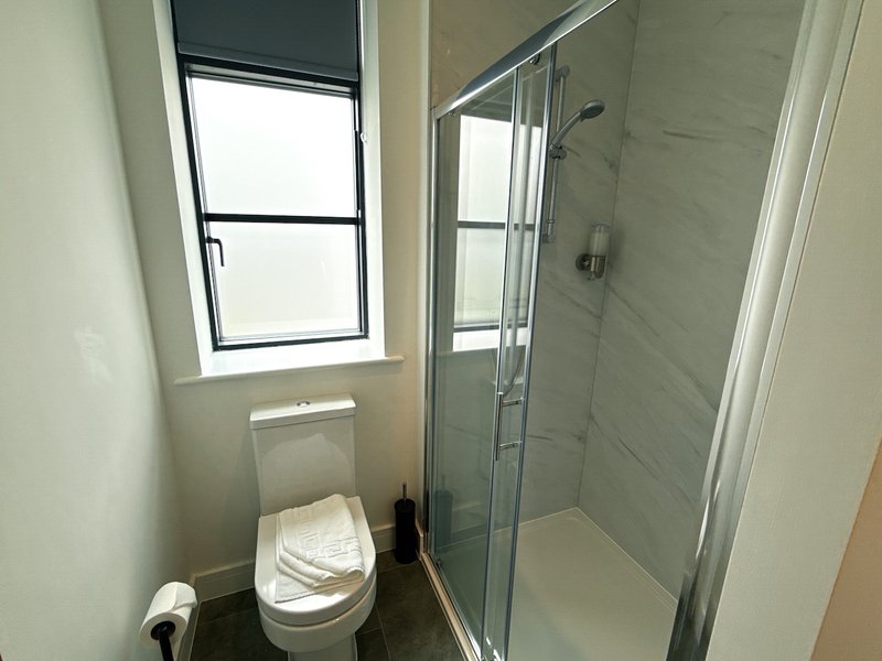 Modern bathroom with toilet, glass shower enclosure, window and neutral tile walls