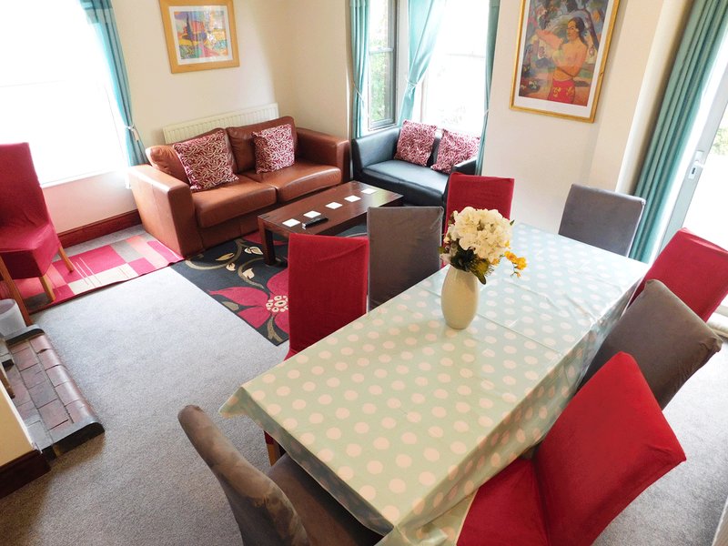 Open-plan living and dining area with brown sofa, red armchairs, dining table and framed wall art
