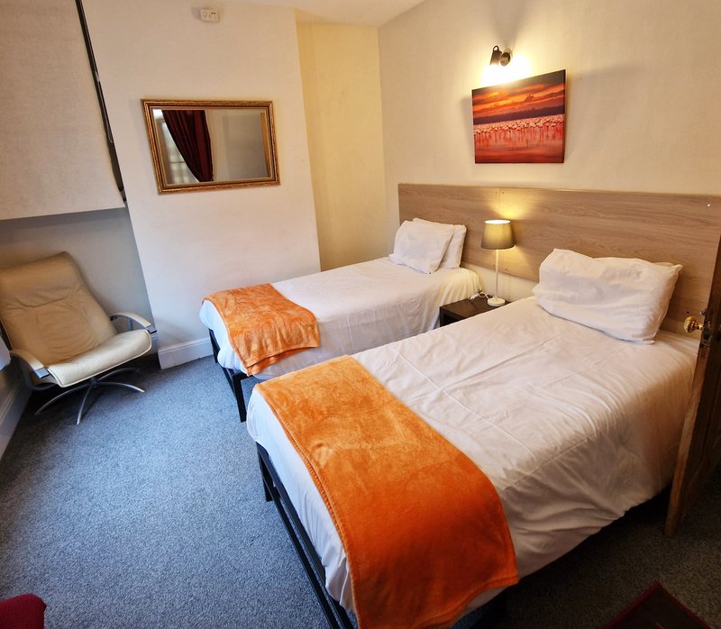 Modern bedroom with two single beds, orange throws, bedside lamps, mirror and wall art