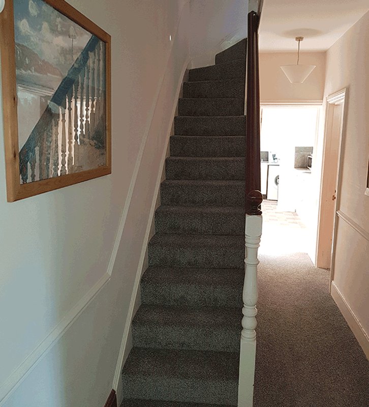 Carpeted staircase with white bannister and framed artwork on wall leading to hallway