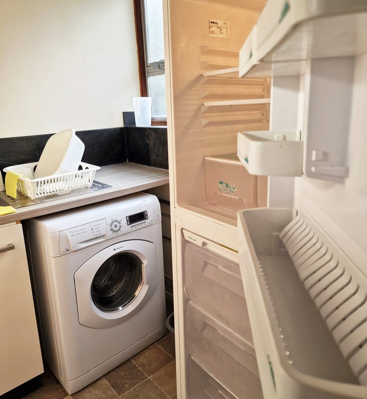 Utility room with white washing machine, open fridge, and storage shelves