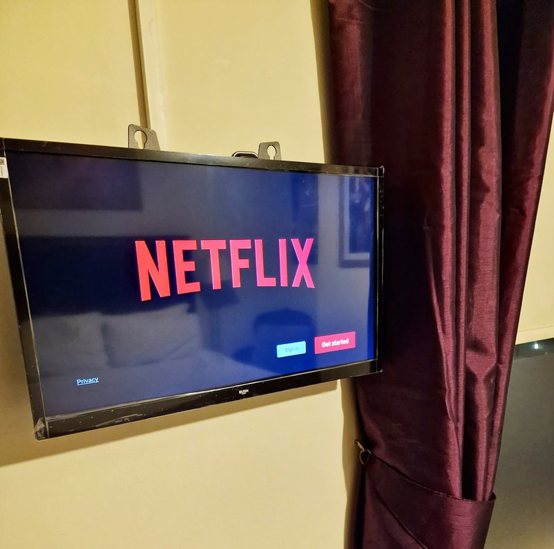 Wall-mounted flat-screen TV displaying Netflix startup screen with burgundy curtain beside