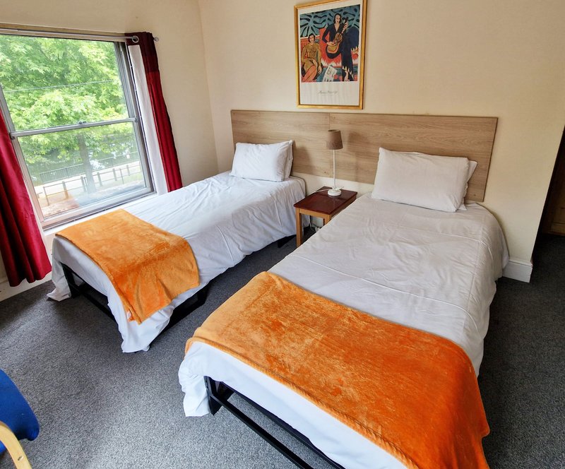 Twin bedroom with two single beds, wooden headboard, orange throws, and window with garden view