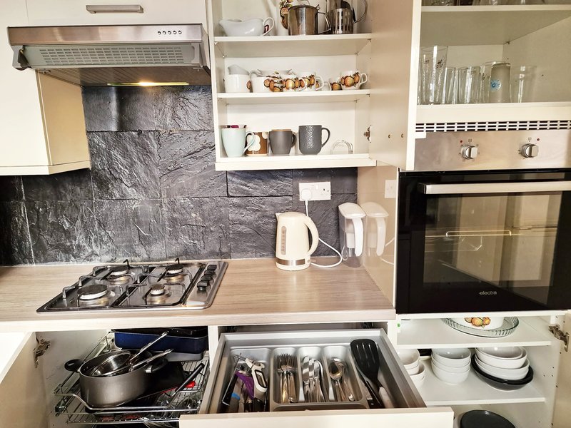 Modern kitchen with gas hob, black splashback, open shelving, and organized drawers