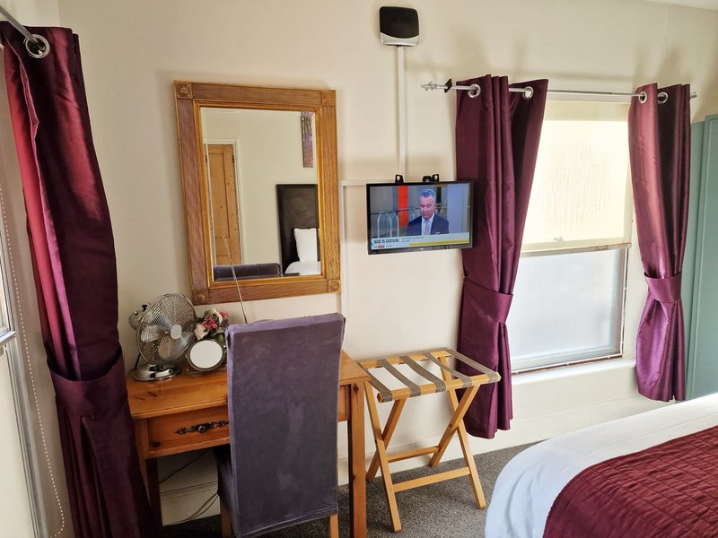 Bedroom with double bed, wooden mirror, TV on wall, purple curtains and desk chair