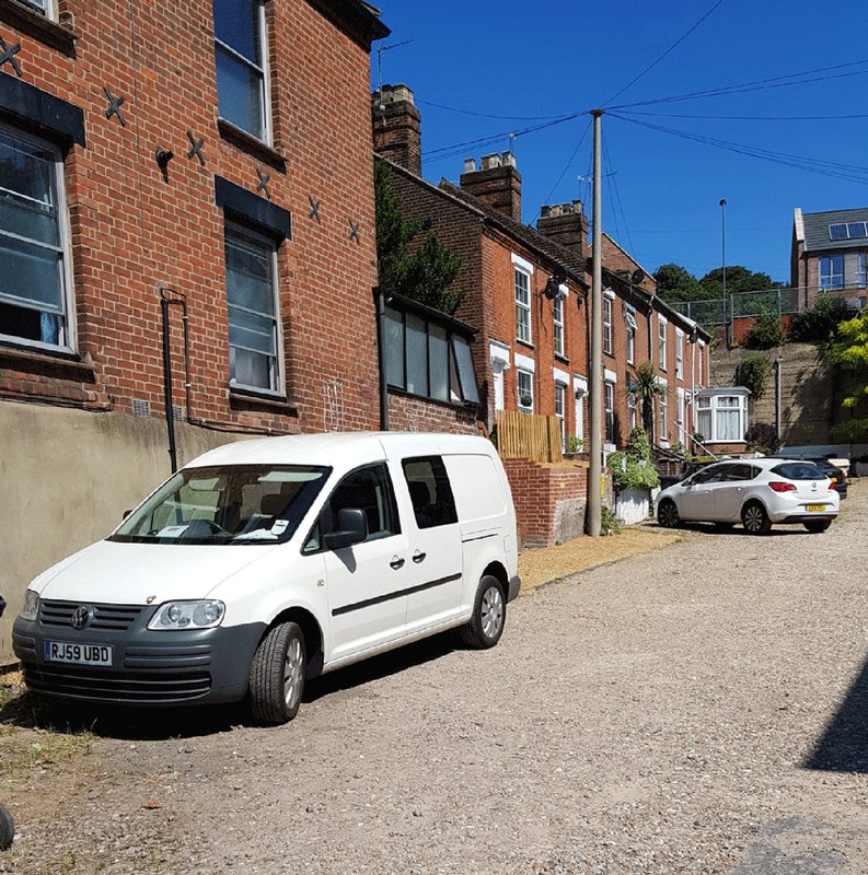 Brick terraced houses with driveway, parked vehicles and clear blue sky