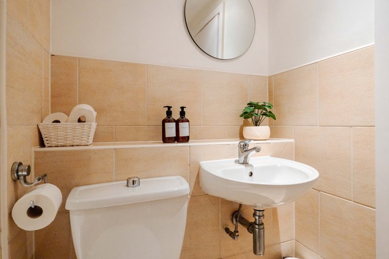 Bathroom with beige tile walls, white toilet, circular mirror, and pedestal sink with plant