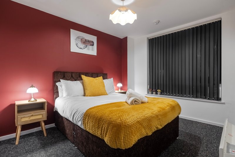 Bedroom with red walls, double bed with yellow bedding, wooden nightstands and ceiling light
