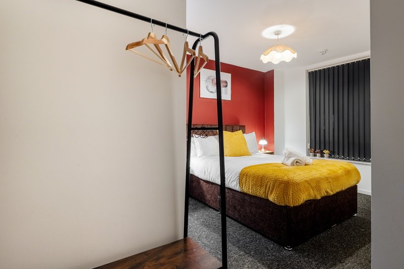 Modern bedroom with black four-poster bed, yellow bedding, red accent wall, wooden hangers on rack