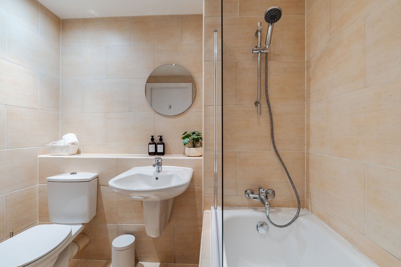 Modern bathroom with pedestal sink, toilet, round mirror, and walk-in shower with rainfall head