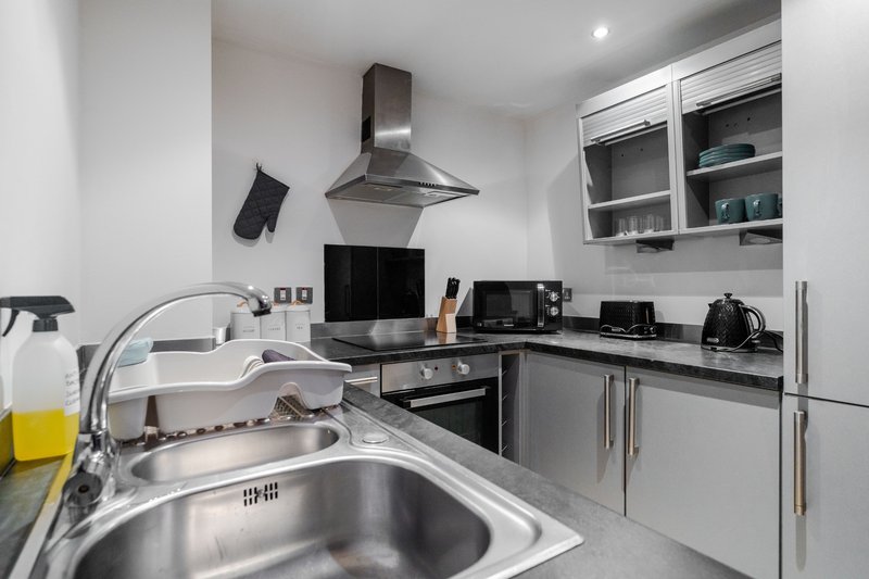 Modern kitchen with stainless steel sink, black countertops, range hood, and integrated appliances