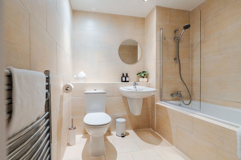 Modern bathroom with toilet, pedestal sink, round mirror, towel rail and bath shower