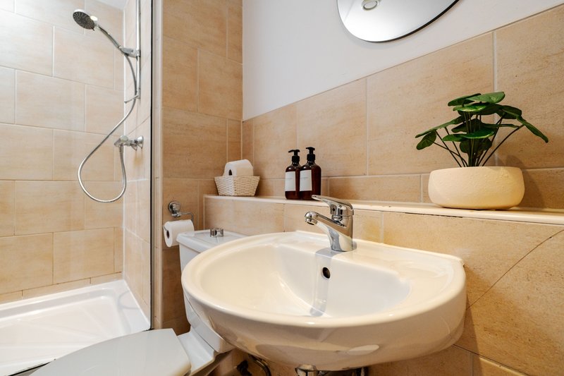 Clean modern bathroom with round sink, shower cubicle, beige tiles, and potted plant
