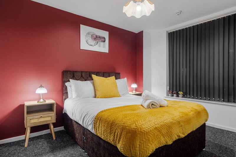 Bedroom with red feature wall, double bed, yellow bedding, wooden bedside table and pendant light