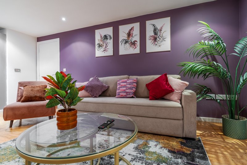 Modern living room with purple walls, beige sofa, potted plants and glass coffee table