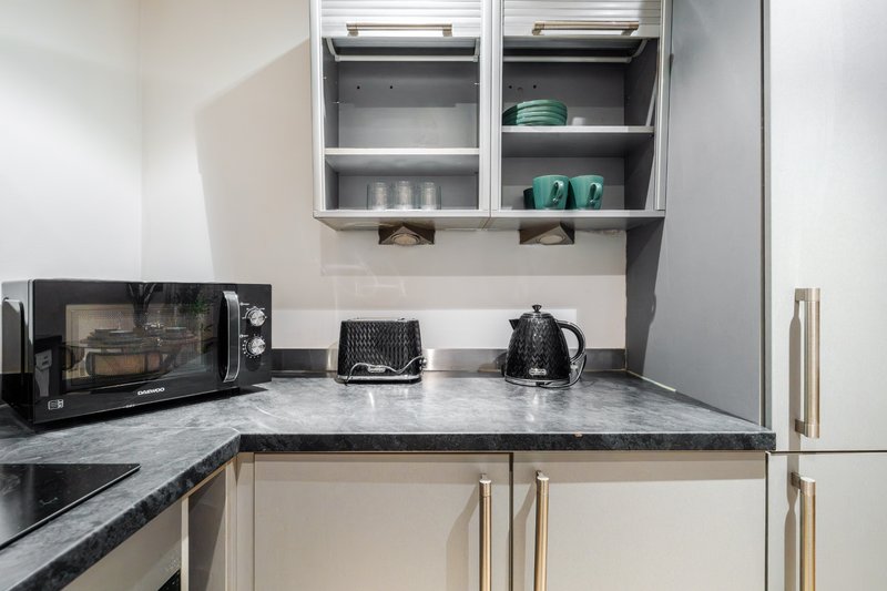 Compact kitchen with marble countertop, microwave, kettle, and wall-mounted storage cupboards