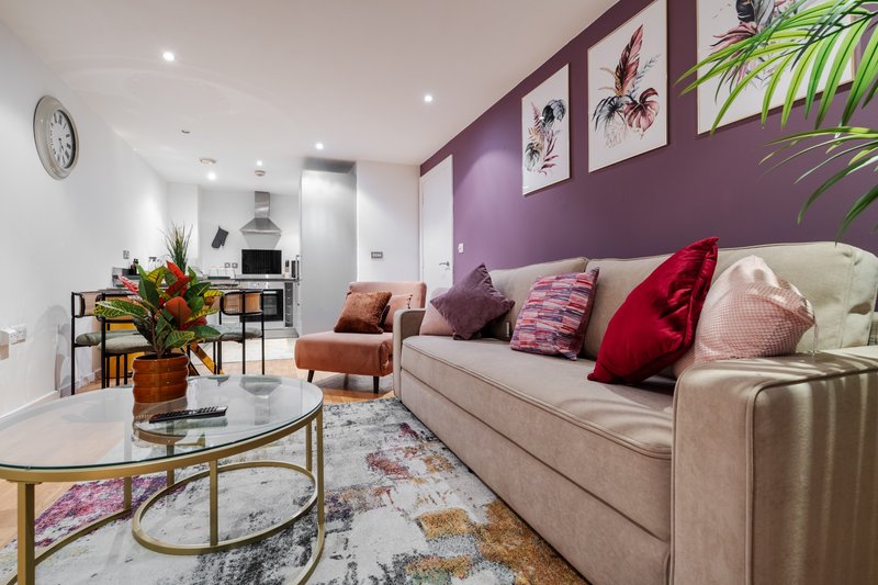 Modern living room with beige sofa, purple accent wall, decorative cushions and framed botanical prints