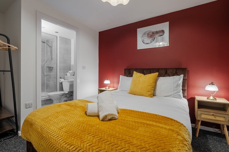 Modern bedroom with double bed, yellow bedding, red accent wall and ensuite bathroom