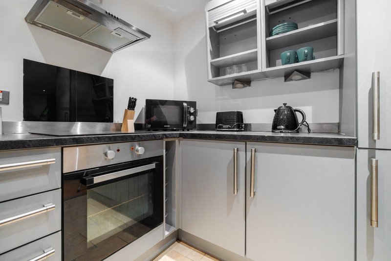 Modern kitchen with white cabinets, stainless steel appliances, black countertop and wall-mounted TV