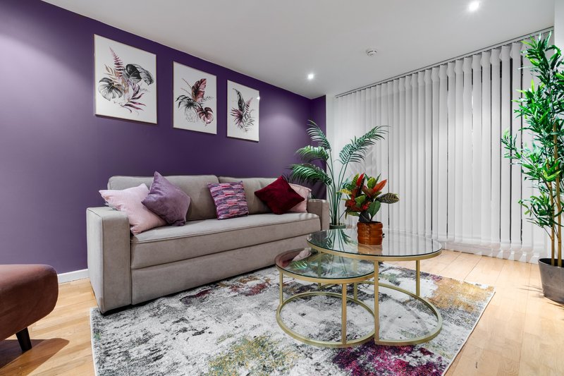 Modern living room with purple accent wall, beige sofa, potted plants and glass coffee table