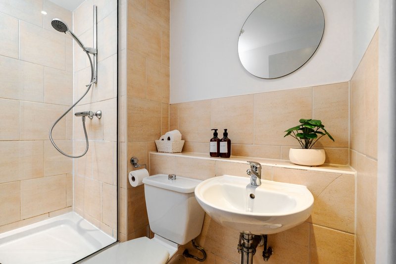 Modern bathroom with shower, white sink, round mirror, and wooden tile accents