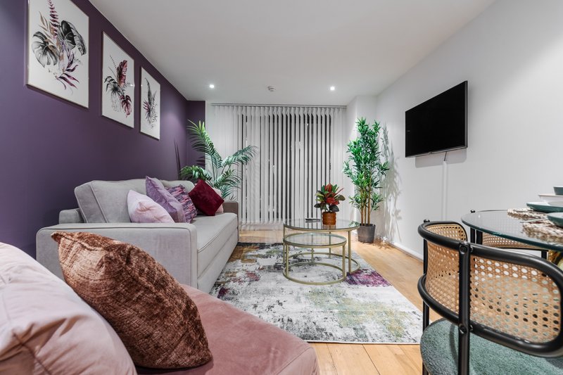 Modern studio apartment with purple accent wall, sofa, potted plants, and mounted TV