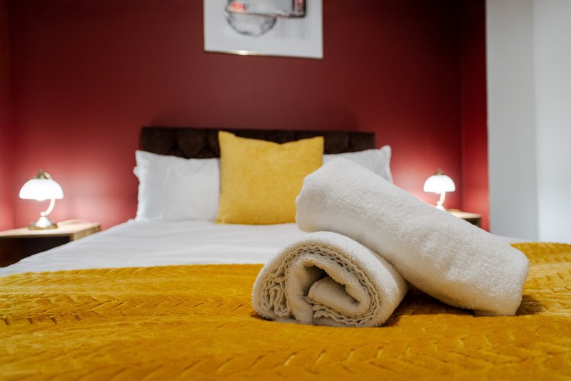 Bedroom with red walls, double bed, rolled towels, yellow bedding and bedside lamps