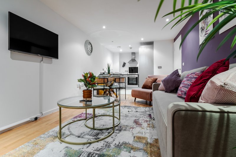 Open-plan living room with sofa, TV, coffee table, kitchen area and plants